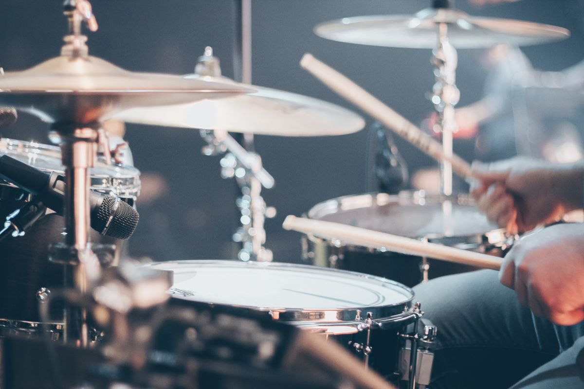Close-up of a drummer playing a drum kit with cymbals and sticks on a darkened stage